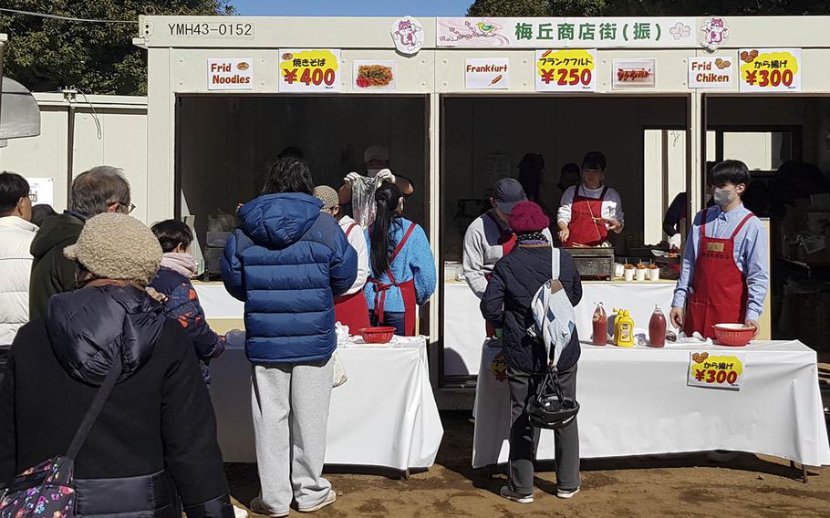 Customers stand in line at tables in front of a snack stand in a Japanese park.