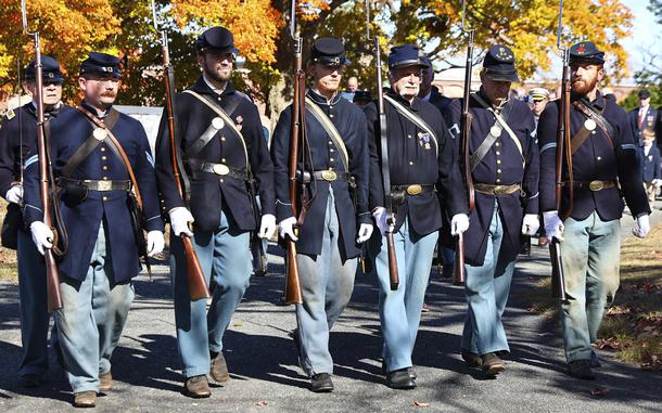 Civil War re-enactors march in a line holding guns while participating in a funeral service.