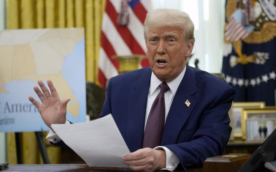 Trump holds a document in his left hand and raises his right as he talks to the media.