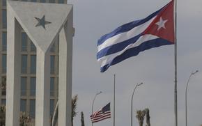 Cuban and American flags fly next to a stone monument with a star.