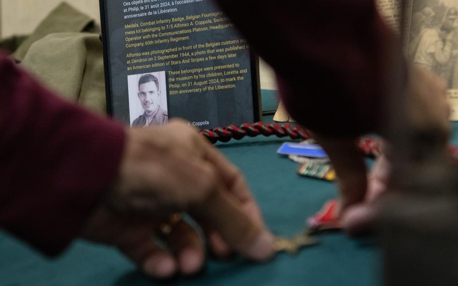 A man sets down medals in front of a museum label with a black-and-white photo of and information on a U.S. soldier. 