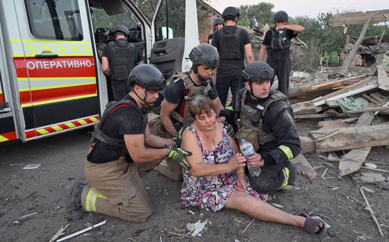 Rescuers assist a woman who fainted outside a destroyed house in Bilopillya, near Russian border.