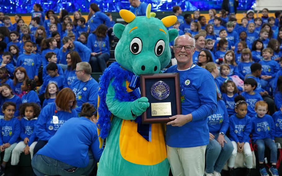 The mascot of Alconbury Elementary School and the school’s principal each hold one side of the Blue Ribbon award plaque.