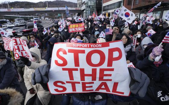 Supporters of impeached South Korean President Yoon Suk Yeol hold a large sign reading, “Stop the Steal,” while others wave South Korean and American flags in the background.