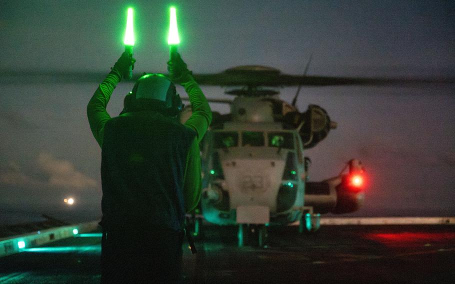 An airman guides a helicopter on the flight deck of the USS Somerset.