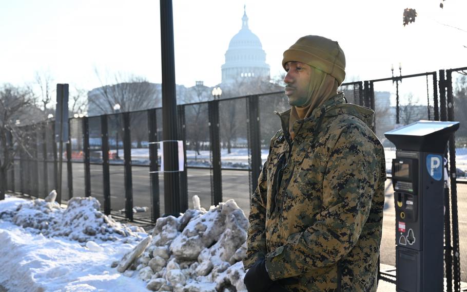 A Marine stands in front of a security fence with the Capitol in the background.