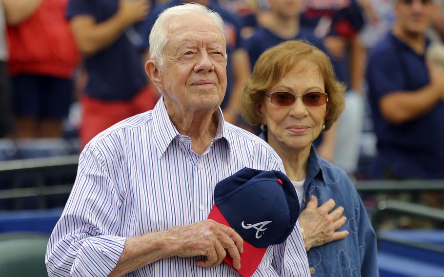 Jimmy Carter places his Atlanta Braves hat on his heart; Rosalynn Carter puts her hand on her heart.