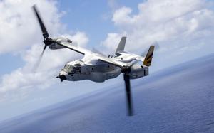 A tiltrotor aircraft is shown with a clear, blue sky and blue ocean horizon in the background.