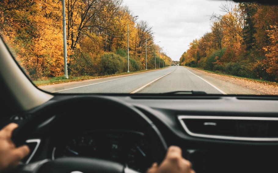 Person driving car on the country road in autumn.