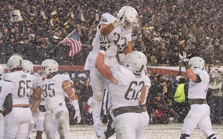 One Army players lifts another into the air after a touchdown on a snowy day.