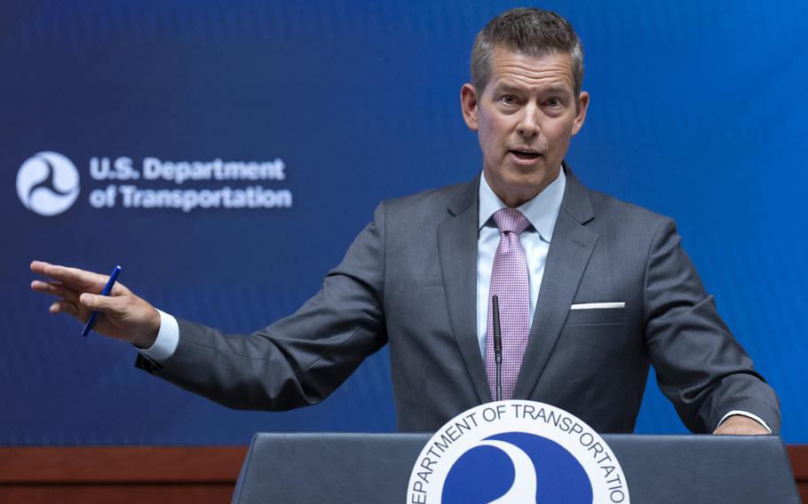 A man in a suit speaks at a podium with one hand extended and holding a pen.