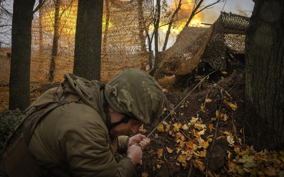 A soldier in combat gear hunches down to fire a large gun from a wooded position.