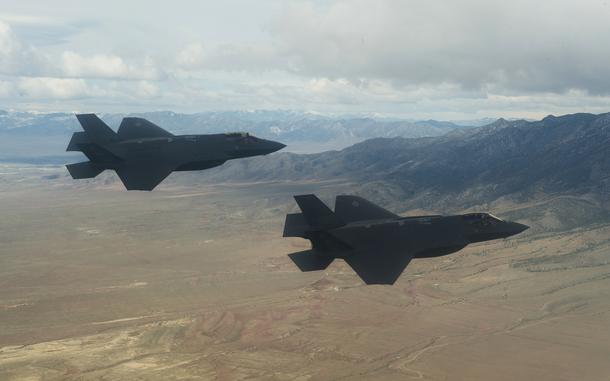 F-35A Lightning II fly with clouds and mountains in the background. 