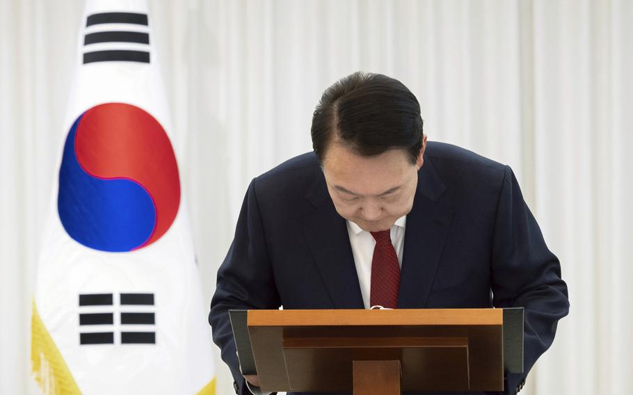 The South Korean president wearing a suit and red tie bows from behind a podium.