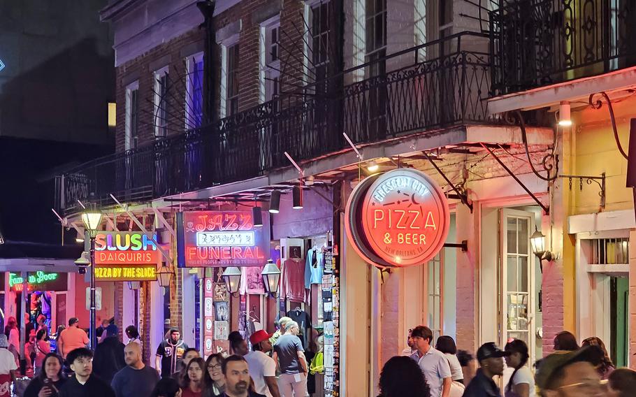 Crowds of people walk in New Orleans amid the nighttime glow of French Quarter restaurant and shop signs.  