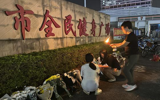 Mourners kneel down to light candles and place flowers on a memorial in front of a stone sign.