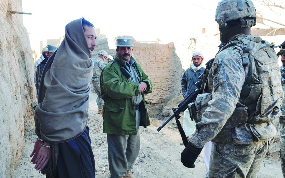 Staff Sgt. Darvin Cosby, 29, of Chicago, right, and Afghan Police Capt. Abdul Zaher, center, guard a suspect arrested by Afghan police as they search his home for bomb-making materials Feb. 9, 2010. 