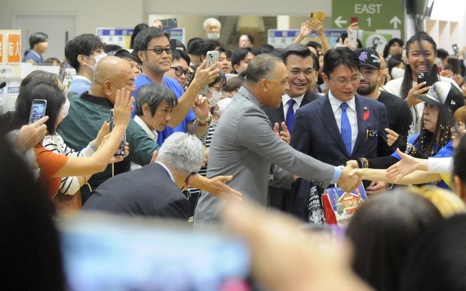 Dave Roberts shakes hands with members of a crowd gathered at Naha city hall.