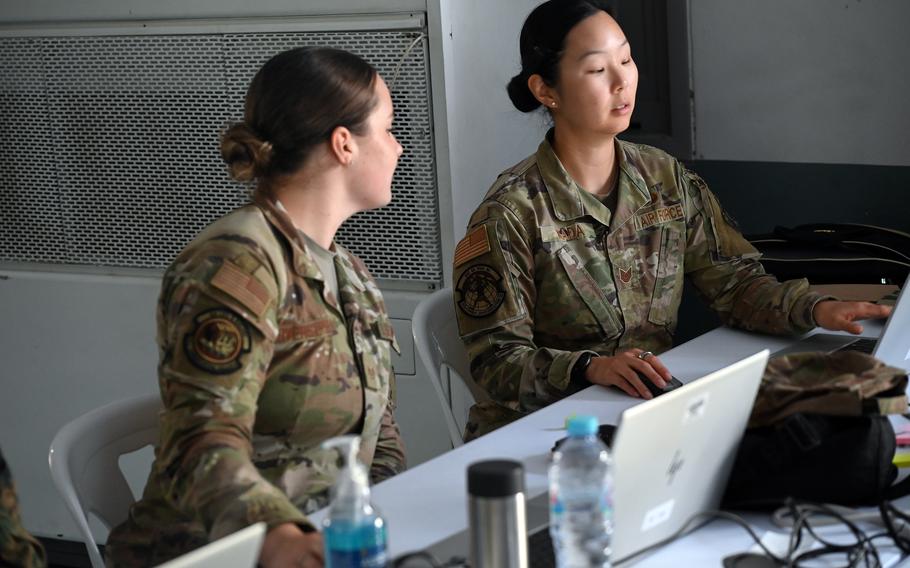 Two female airmen talk while looking at a computer screen.