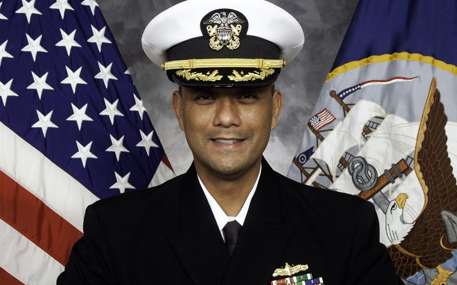 A man dressed in a Navy uniform smiles for a professional headshot.