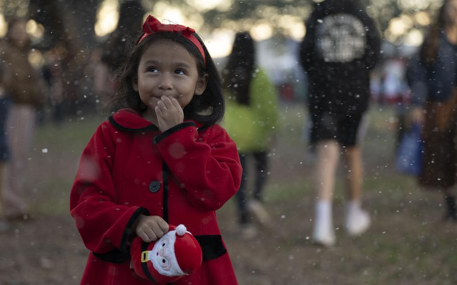 A young girl in a red coat holding a Santa Claus enjoys MacWonderland at MacDill Air Force Base.