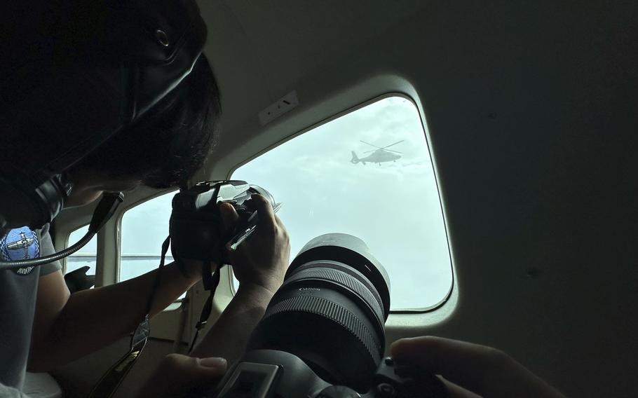 Photographers in an aircraft take pictures through a window of a passing military helicopter.