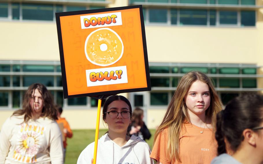 A girl holds an orange sign with a doughnut on it that reads “Donut Bully.”