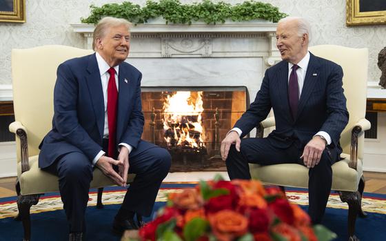 Joe Biden and Donald Trump sit next to each in chairs in front of a fireplace in the Oval Office of the White House.