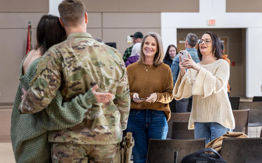 A male soldier and a woman are seen from behind embracing for a photo, while two others take their picture.