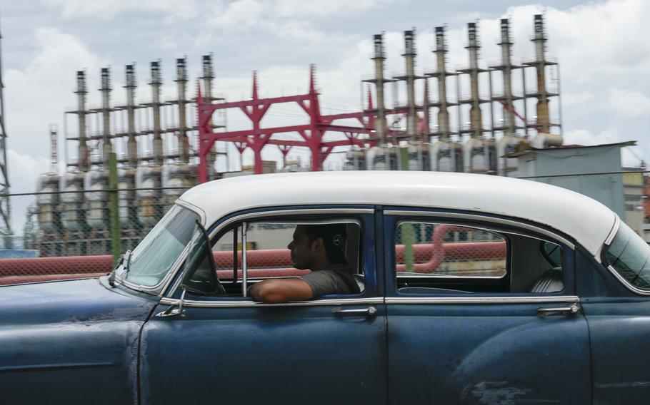 A man drives a classic American car with a floating power generator in the background.