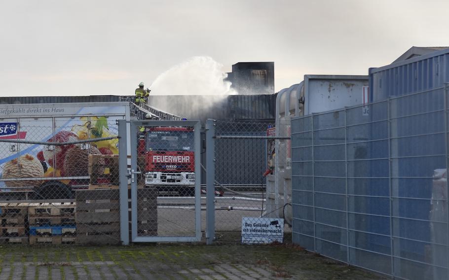 A fence in the foreground and a firefighter spraying water in the background.