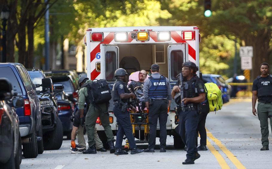 A man with a bloody face is loaded onto a stretcher into an ambulance by armed police officers and medics.