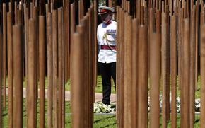 A servicemember with a white and black uniform stands in the center of the photo in the middle of a new memorial that consists of many wooden poles.