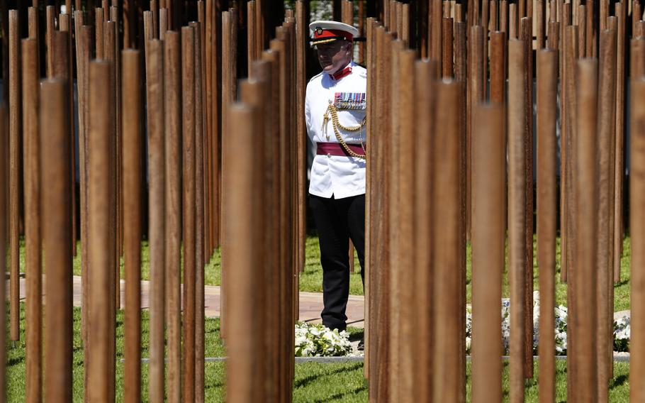 A servicemember with a white and black uniform stands in the center of the photo in the middle of a new memorial that consists of many wooden poles.