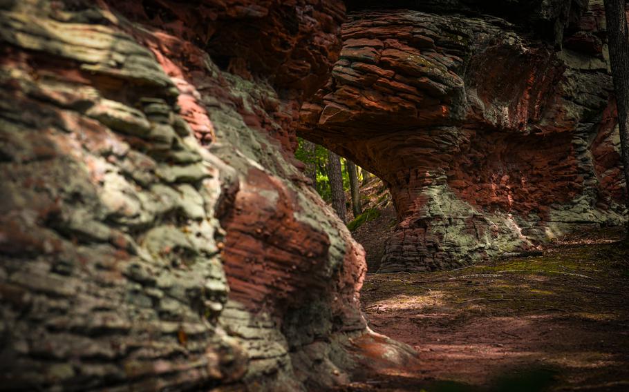 A path winds between two colorful sandstone walls near Ludwigswinkel, Germany. The Rumbergsteig hiking trail offers easy access to hikers of all skill levels.