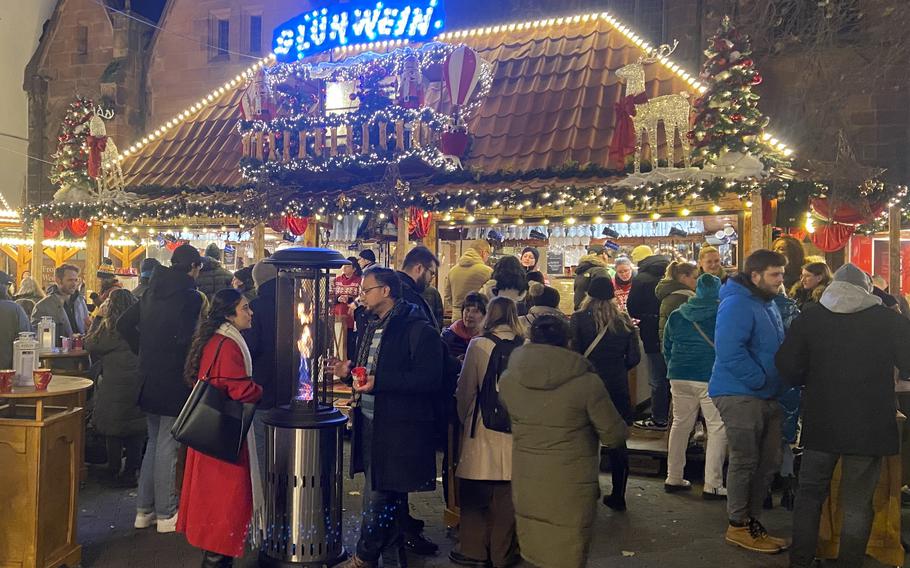 People dressed in winter coats gather around a stand with a lighted sign that says “gluehwein.”