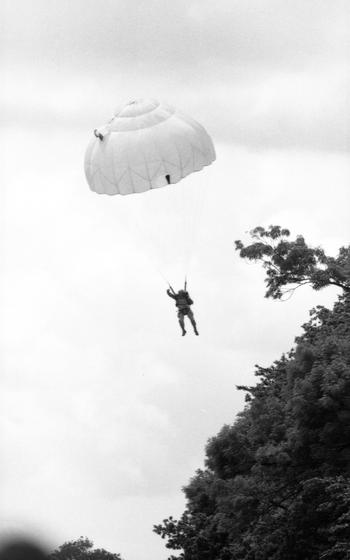 A paratrooper glides towards solid ground as he lands. 