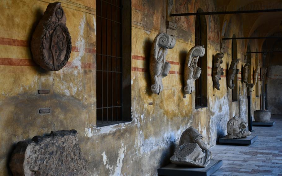 Stone statues and flourishes hang on a yellow paint-peeled wall outside the Museo Civico in Bassano del Grappa, Italy