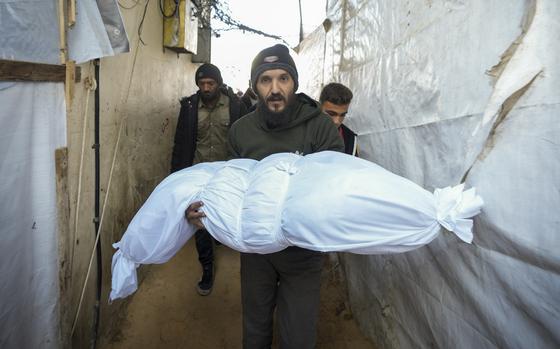 A man carries a body wrapped in a white sheet.