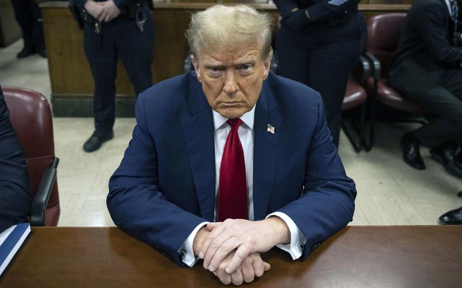 Donald Trump sits at a courtroom table with his hands folded in front of him.