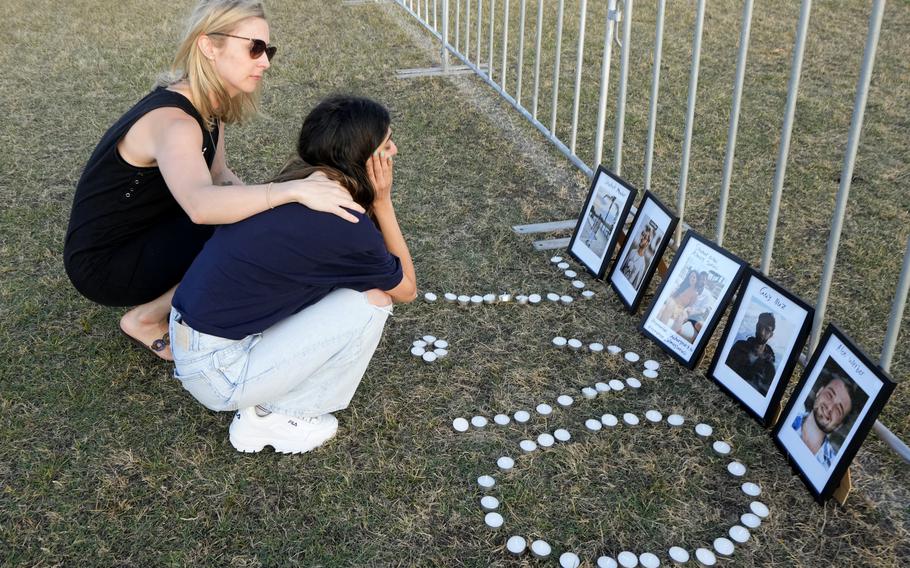 Two women console each other in front of a photo memorial at a park in Sydney, Australia.