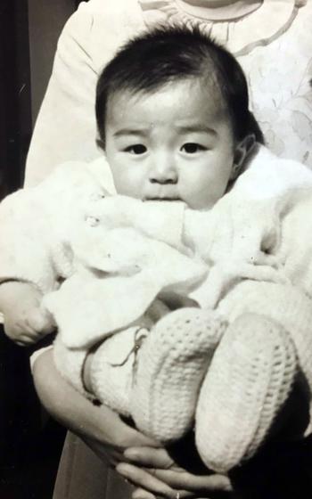 A black and white picture of a baby wearing a white outfit. 