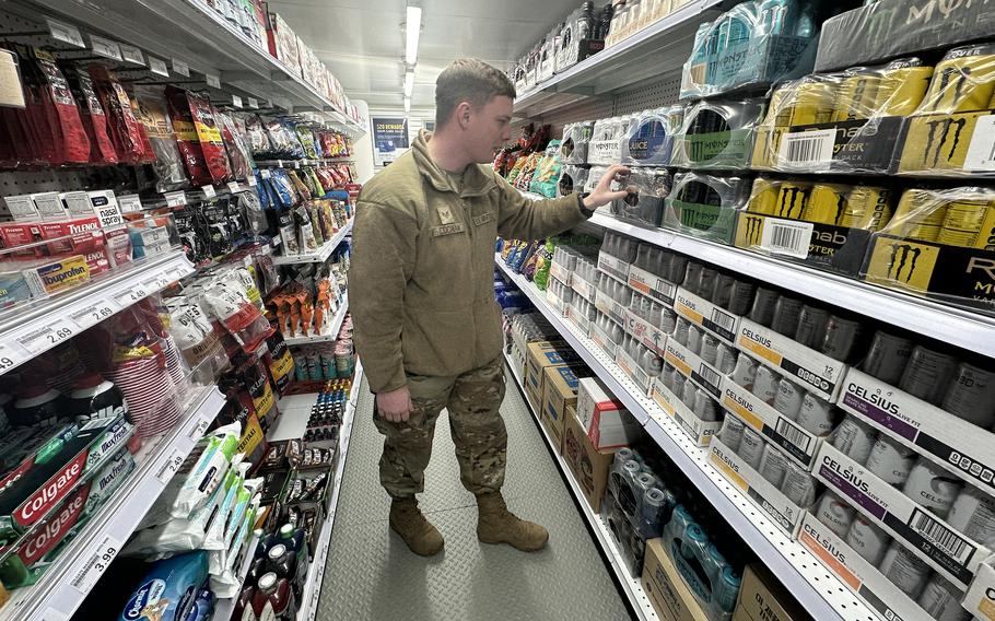 An airman in camouflage uniform looks at energy drinks on a store shelf.