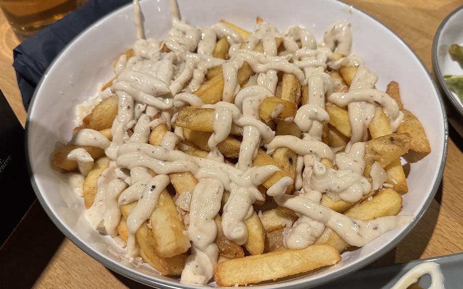 Steak fries are abundantly covered with a creamy-looking sauce on a plate.