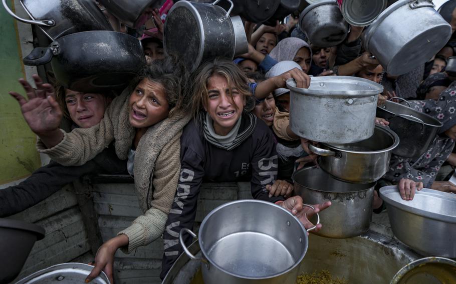 A mass of people extend empty pots and buckets outward for food.