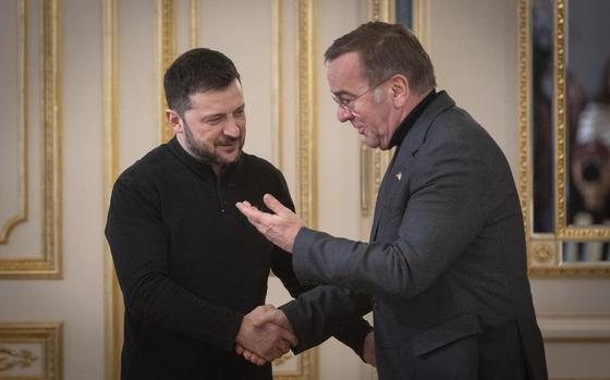 Volodymyr Zelenskyy, left, shakes hands with Boris Pistorius, who is smiling and raising his other hand in greeting.