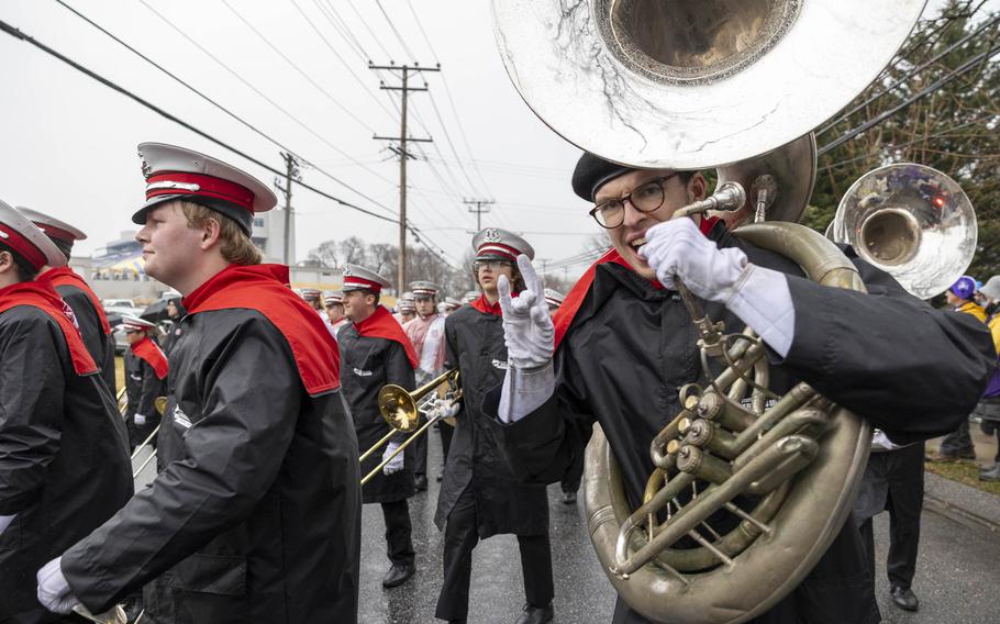 A man in a marching band uniform holding a tuba flashes the sign of the horns.