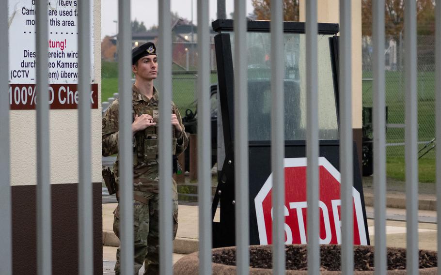 An airman in uniform stands behind the bars of the main gate at Spangdahlem Air Base.