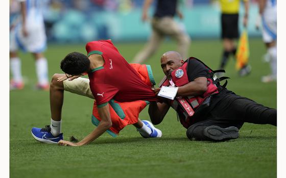 A steward catches a pitch invader during the men's Group B soccer match between Argentina and Morocco at Geoffroy-Guichard Stadium at the 2024 Summer Olympics, Wednesday, July 24, 2024, in Saint-Etienne, France. (AP Photo/Silvia Izquierdo)