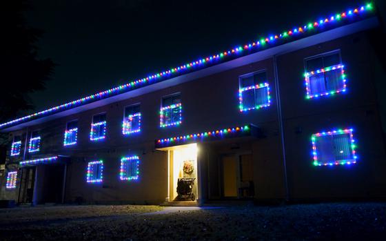 A house illuminated at night with strings of multi-colored Christmas lights around the windows and along the roof.